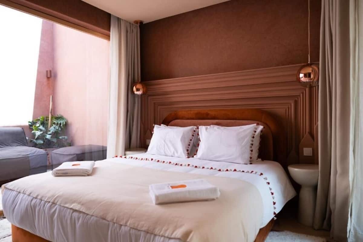 Une chambre d’hôtel avec un grand lit, une petite table, un canapé et une fenêtre avec des rideaux.