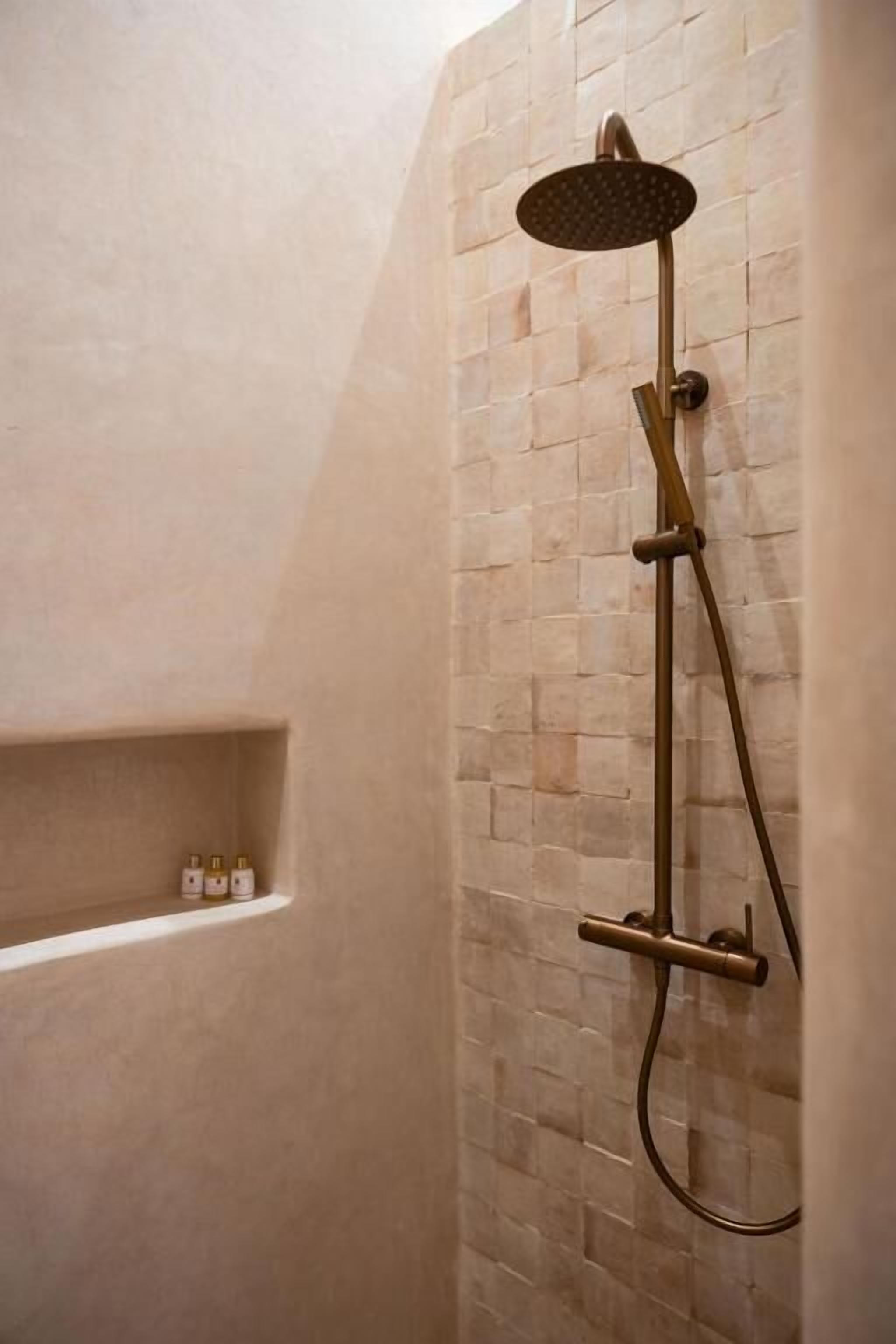 A shower with a handheld showerhead mounted on a wall with a brick pattern.