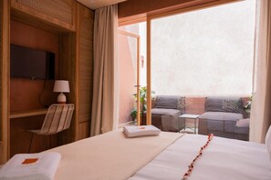 A hotel room with a bed, a chair, a small table, a TV, and a balcony with seating.