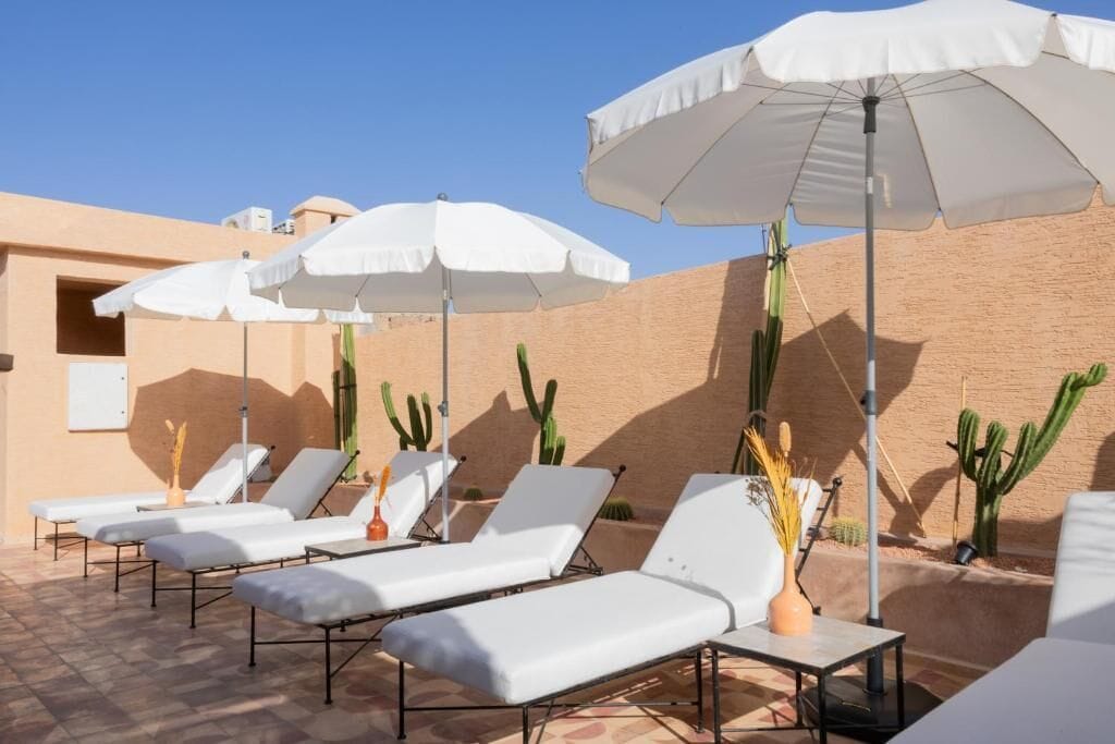 A sunlit outdoor lounge area with white lounge chairs and umbrellas, surrounded by cacti.