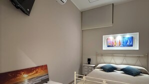 Un dormitorio con una cama, mesitas de noche, un televisor montado en la pared y obras de arte.