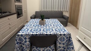 Una cocina moderna con electrodomésticos integrados, una mesa de comedor con mantel estampado, un sofá gris y una planta en maceta.