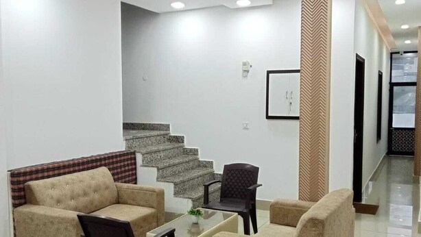 Una sala de estar moderna con un sofá, una mesa de centro y una silla. Se ve una escalera que sube a otro nivel.