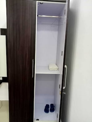 Un armario con barra para colgar, un estante con una toalla doblada y un par de zapatos.