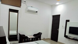 Habitación de hotel con cama, escritorio, dos sillas, televisión y aire acondicionado.
