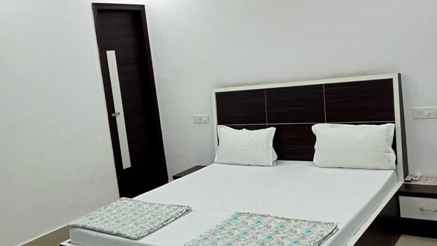 A bedroom with a bed, bedside tables, a ceiling fan, and a door. - Hotel Paul Residency  (Malout)