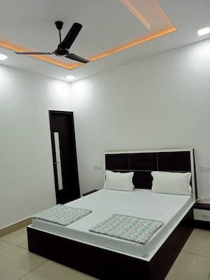 Un dormitorio con cama, ventilador de techo, una puerta y una mesita de noche.