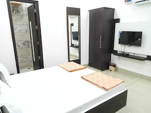 Un dormitorio con cama, armario, espejo, televisor y un taburete pequeño.