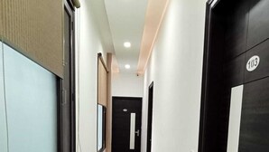 Un pasillo limpio y bien iluminado con suelo de baldosas, una puerta negra con un número y una ventana con persianas.