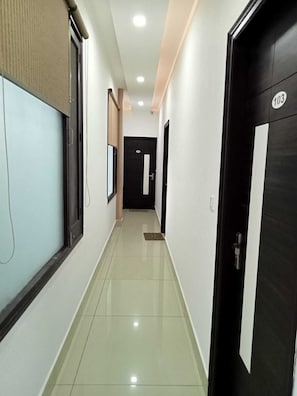 A clean, well-lit hallway with a tiled floor, a black door with a number, and a window with blinds.