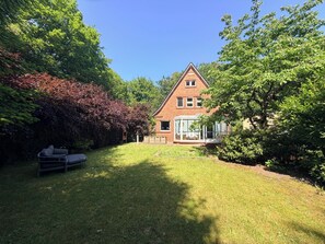 Ein Haus mit Wintergarten, umgeben von einer gepflegten Rasenfläche und dichtem Grün.