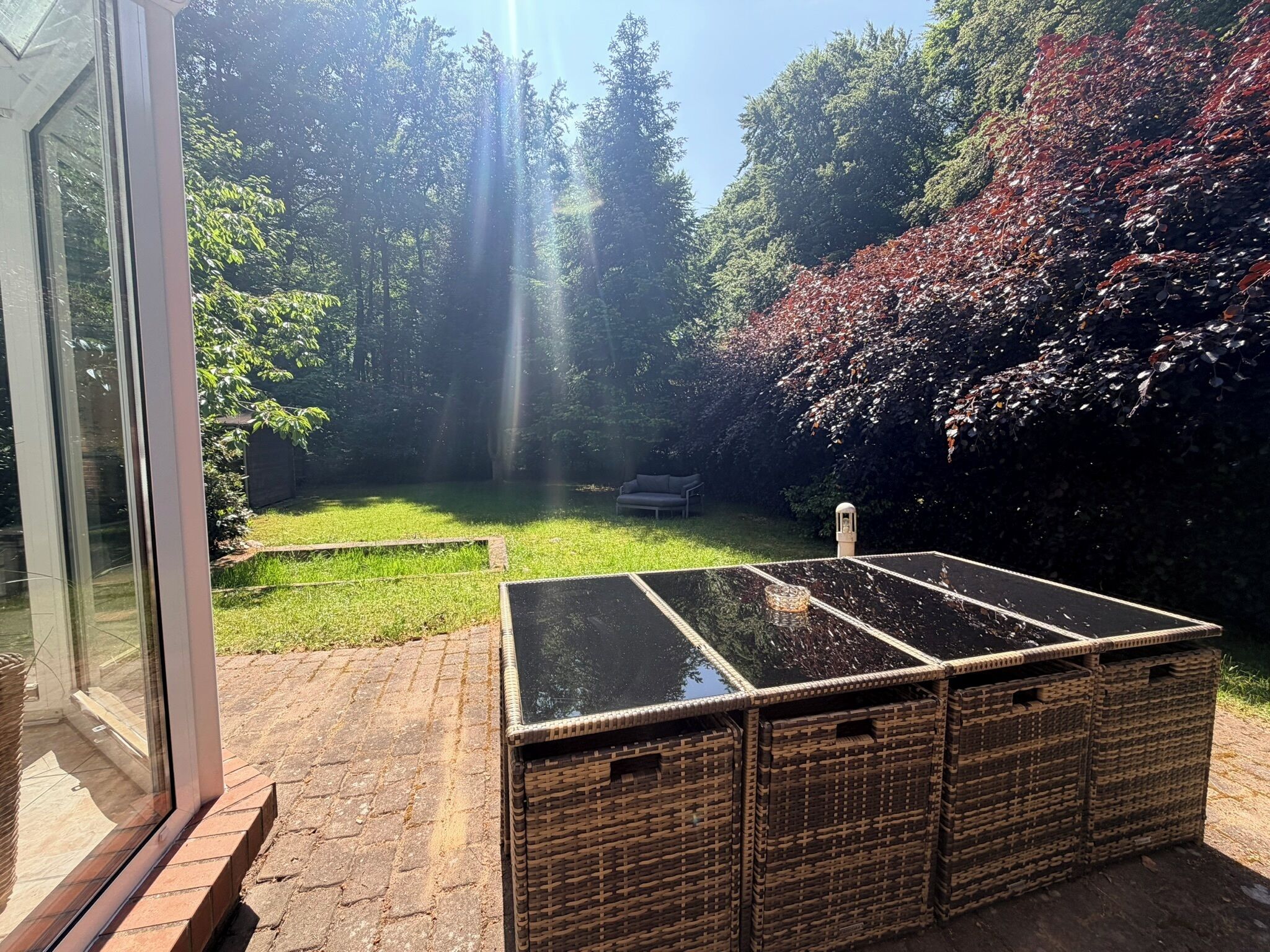 Een terras met een glazen deur, een rieten tafel en een gazon.