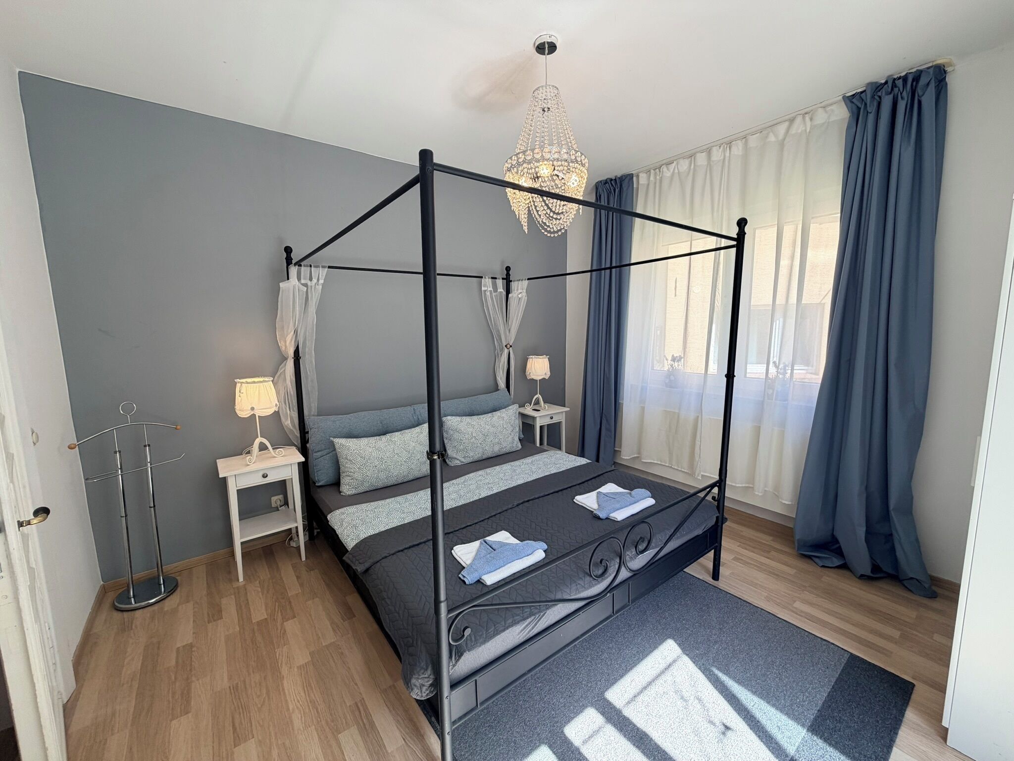Een hemelbed met een baldakijn, nachtkastjes met lampen, een kroonluchter en uitzicht naar buiten door een raam met gordijnen.