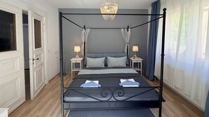 A four-poster bed with a canopy, bedside tables with lamps, a chandelier, and a view of the outdoors through sheer curtains. - Holiday home Wald & Welle: Your paradise between beach and nature (Graal-Müritz)