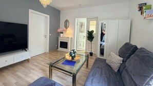 A living room with a TV, sofa, glass coffee table, fireplace, and chandelier. - Holiday home Wald & Welle: Your paradise between beach and nature (Graal-Müritz)