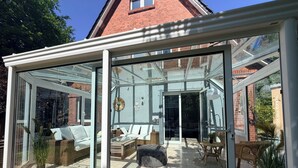 A conservatory with glass walls, a brick house, and outdoor furniture. - Holiday home Wald & Welle: Your paradise between beach and nature (Graal-Müritz)