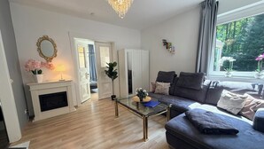 A living room with a fireplace, a sofa, a glass coffee table, and a chandelier. - Holiday home Wald & Welle: Your paradise between beach and nature (Graal-Müritz)