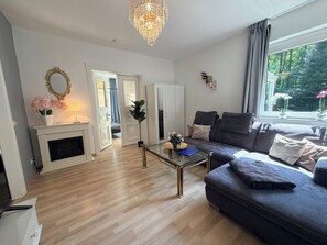 Een woonkamer met een open haard, een bank, een glazen salontafel en een kroonluchter.