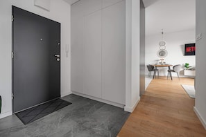 Ein modernes Interieur mit einer dunklen Tür, grauen Fliesenboden, einem Essbereich mit Tisch und Stühlen sowie einem an der Wand befestigten Fernseher.