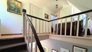 Eine Treppe mit dunkler Handlauf und weißen Spindeln, die zu einer zweiten Etage mit einer Tür und einem gerahmten Bild an der Wand führt.