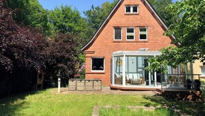 Ein Ziegelhaus mit Wintergarten, einem kleinen Garten und einem strahlend blauen Himmel.