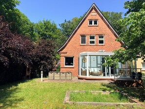 Ein Ziegelhaus mit Wintergarten, einem kleinen Garten und einem strahlend blauen Himmel.