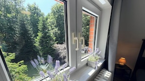 Ein Zimmer mit Blick auf einen Wald durch ein Fenster, ein Heizkörper und eine Lampe auf einem Nachttisch.