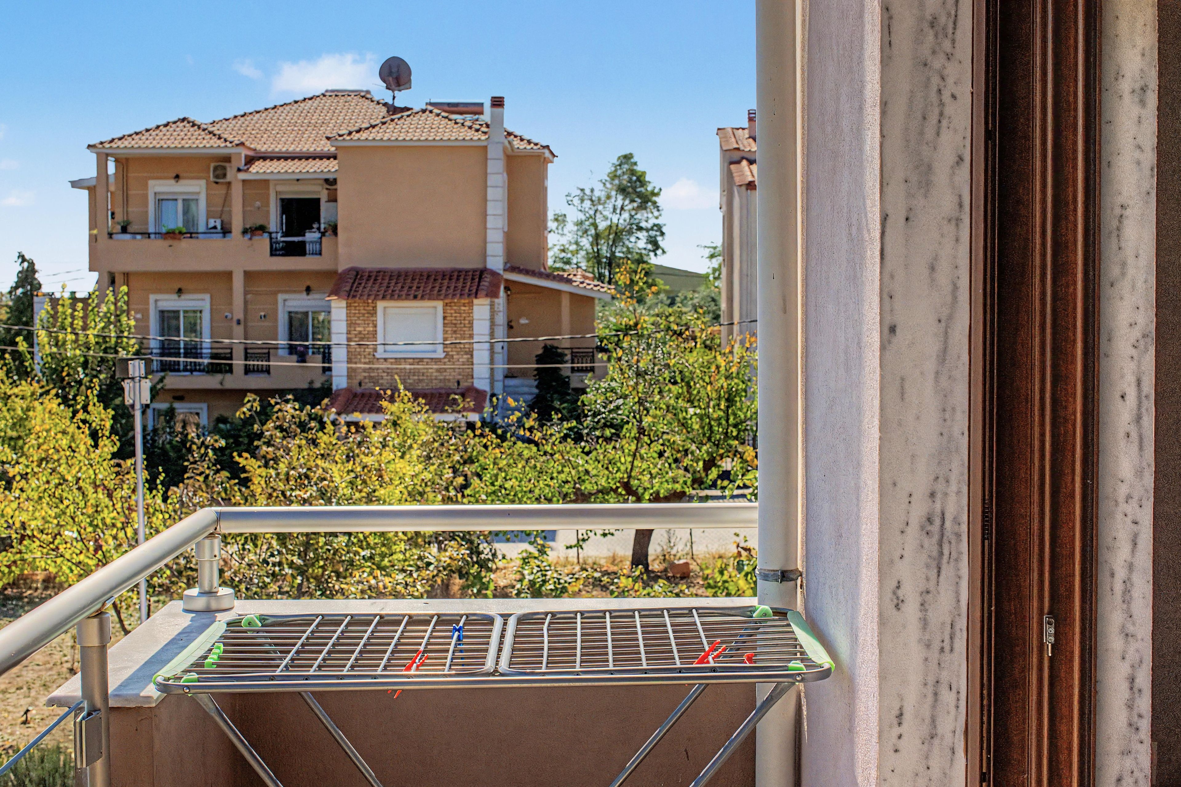 Un balcón con un tendedero metálico y un edificio con varios balcones al fondo.