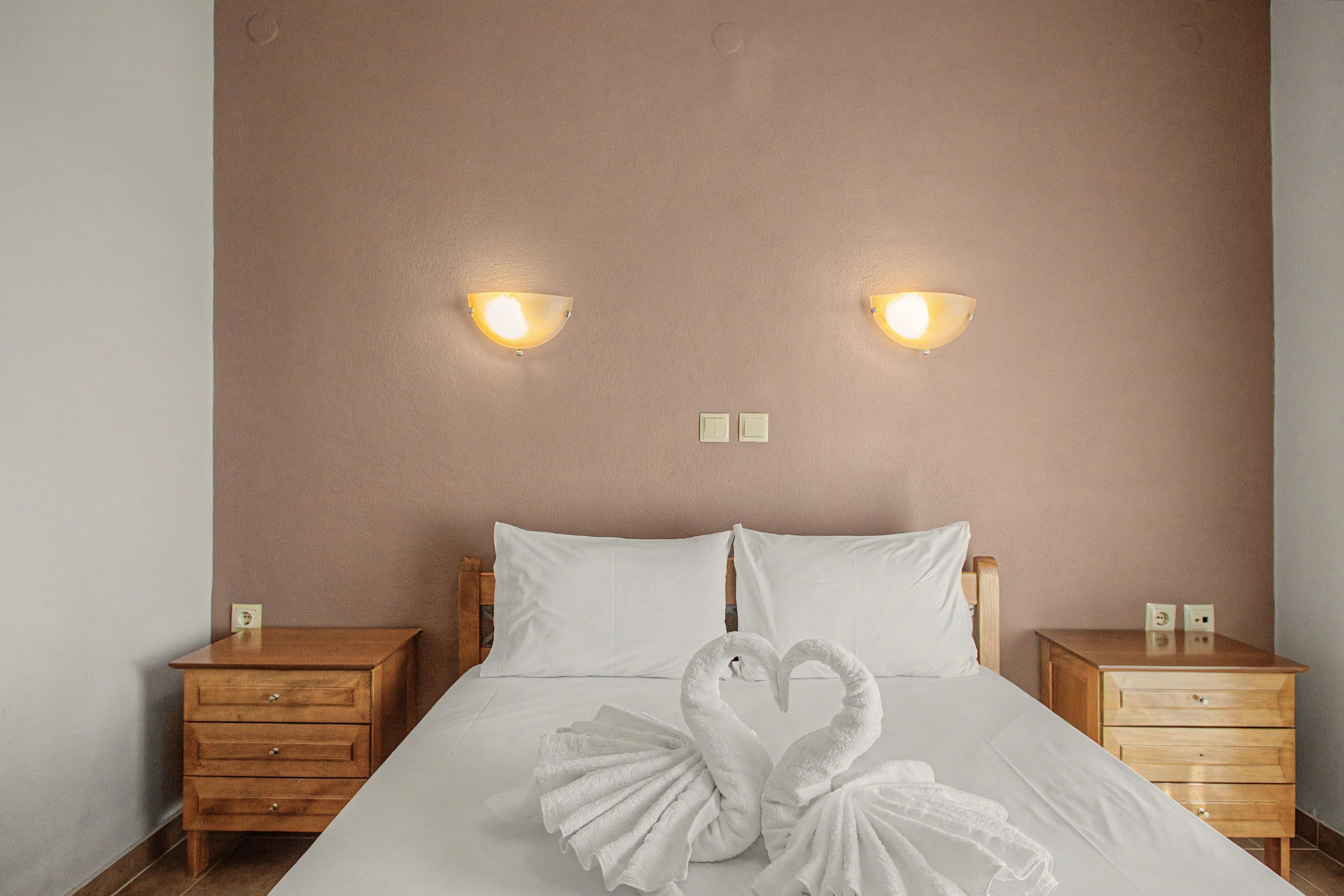 A hotel room with a bed, two nightstands, and wall-mounted lighting.
