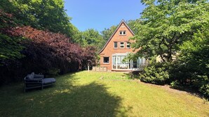 Ein Haus mit Wintergarten, umgeben von einer gepflegten Rasenfläche und dichtem Grün.