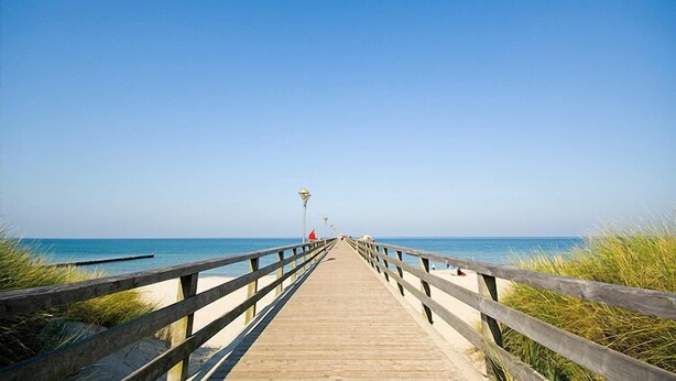 Eine Holzstege führt zu einem Strand unter blauem Himmel.