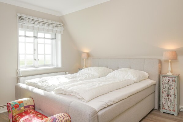 A bedroom with a bed, a window with curtains, a chair, and a bedside table with a lamp. - Haubarg Ossenhoff apartment for 6 persons near St.Peter-Ording (Tating)
