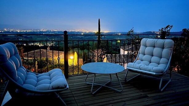 Varanda com duas cadeiras brancas acolchoadas e uma mesa redonda pequena, com vista para o horizonte urbano ao entardecer.