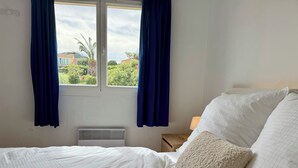 Quarto com cama, janela com cortinas, mesa de cabeceira com abajur e radiador.