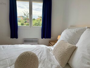 Ein Schlafzimmer mit Bett, einem Fenster mit Vorhängen, einem Nachttisch mit Lampe und einer Heizung.