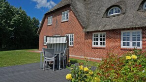 A red brick house with a thatched roof, a patio with a table and chairs, and a garden with yellow flowers. - Historic Haubarg close to the North Sea near St. Peter-Ording for 7 people (Tating)