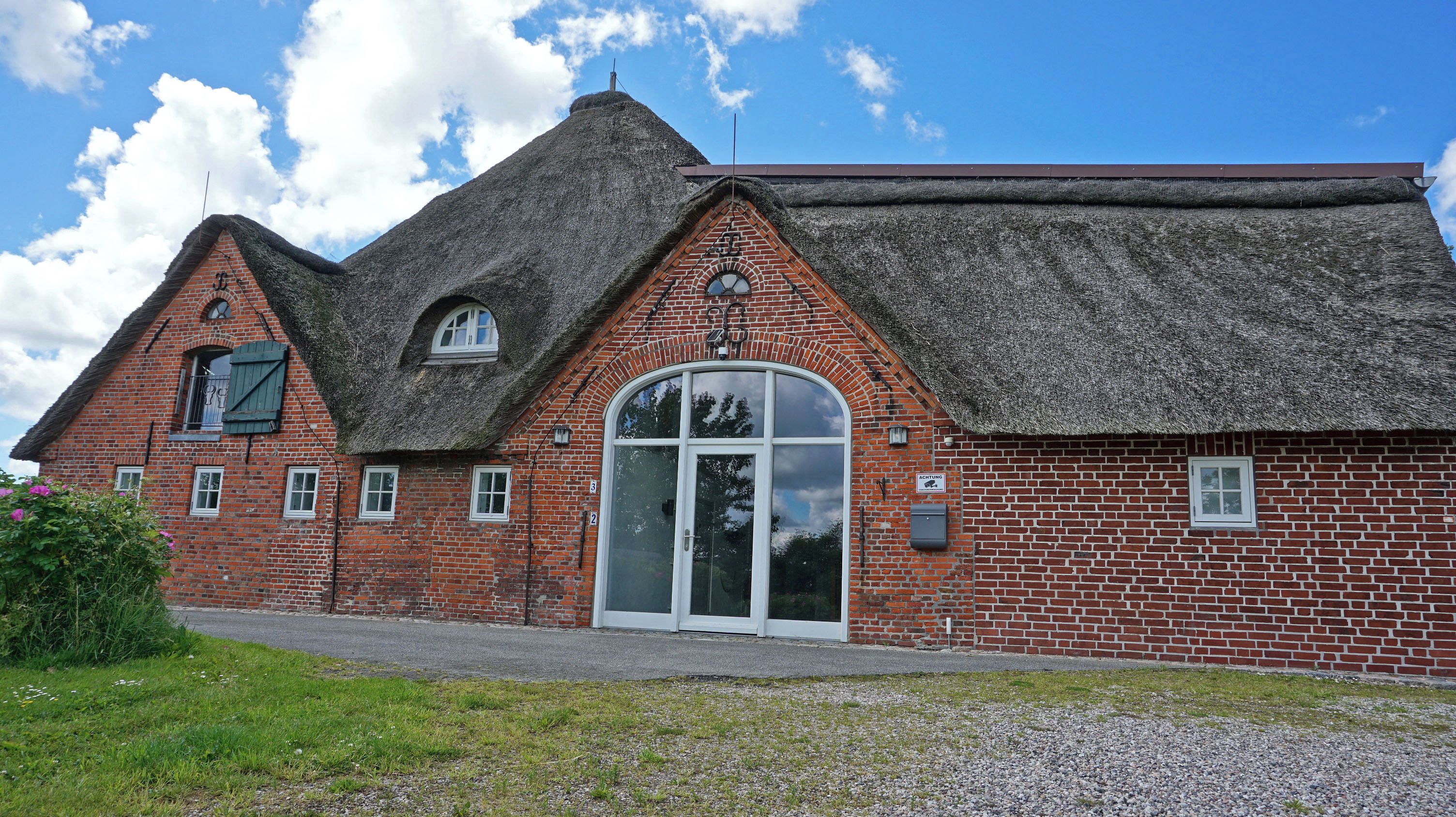 A brick building with a thatched roof, a large arched entrance, and a small balcony.