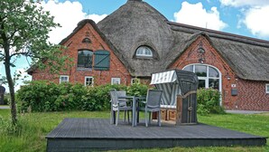 A brick building with a thatched roof, a small garden with chairs and a table, and a clear sky. - Apartment for 3 in a cozy Haubarg near St.Peter-Ording (Tating)