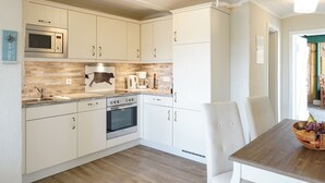 A modern kitchen with white cabinets, a microwave, stove, and a dining area with a wooden table and chairs. - Apartment for 3 in a cozy Haubarg near St.Peter-Ording (Tating)