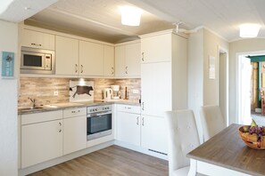 Eine moderne Küche mit weißen Schränken, einer Mikrowelle, einem Herd und einem Essbereich mit einem Holztisch und Stühlen.