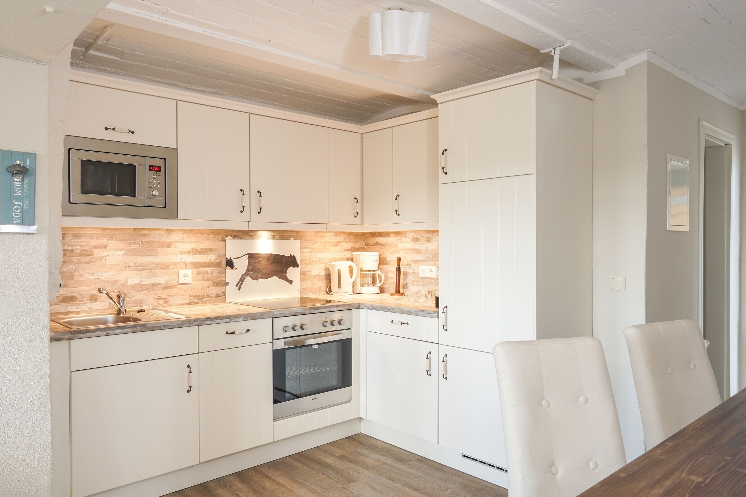 A kitchen with white cabinets, a microwave, an oven, a sink, and a dining table with chairs.