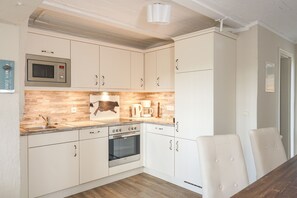 Eine Küche mit weißen Schränken, einer Mikrowelle, einem Backofen, einem Spülbecken und einem Esstisch mit Stühlen.