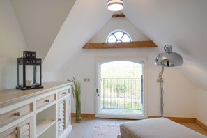 A bedroom with a sloped ceiling, a bed, a desk with drawers, a lamp, and a window with a view of the outdoors. - Cozy vacation apartment in Haubarg for 4 near North Sea & St. Peter-Ording (Tating)