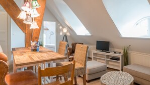 Ein Loft-Zimmer mit Holztisch, Korbstühlen, einem Fernseher auf einem weißen Schrank und einem Oberlicht.