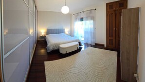 A bedroom with two beds, a large window with curtains, a wooden wardrobe, and a round ceiling light. - XL house for large tribes in the heart of nature, quick access to Parc Gerês (Braga)