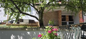 Un espace patio aménagé avec des meubles en osier, un arbre et des fleurs roses.