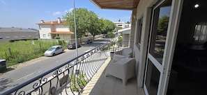 Un balcon donnant sur une rue, une voiture garée et un immeuble avec un toit rouge.