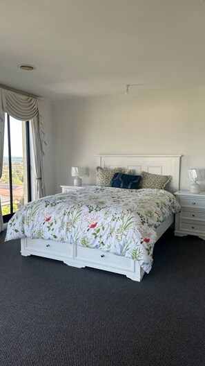 A bedroom with a large bed, two bedside tables, a window with curtains, and a view of the outside.