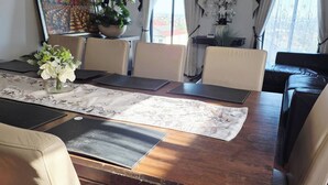 A dining room with a wooden table, beige chairs, a vase of flowers, a painting on the wall, and a view through the window. - Panoramic View in Narre Warren North (Melbourne)