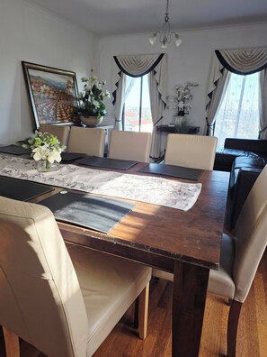 A dining room with a wooden table, beige chairs, a vase of flowers, a painting on the wall, and a view through the window. - Panoramic View in Narre Warren North (Melbourne)
